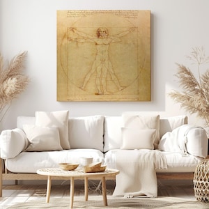 Op de afbeelding: Een ingelijste print van Leonardo da Vinci's Vitruviusman, met een mannelijke figuur in een cirkel en een vierkant. Het kunstwerk is in sepiatinten, gemonteerd op een muur boven een witte bank en een houten salontafel.