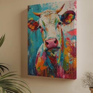 Puede incluir: Una pintura colorida de la cara de una vaca. La obra presenta una vaca blanca con una nariz rosa y cuernos. El fondo es una mezcla de pinceladas azules, rosas, naranjas y amarillas, creando una pieza vibrante y expresiva.