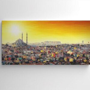 May include: A canvas print of a cityscape at sunset. The image features a large mosque with two minarets, set against a vibrant orange and yellow sky. The city below is a mix of colorful buildings.