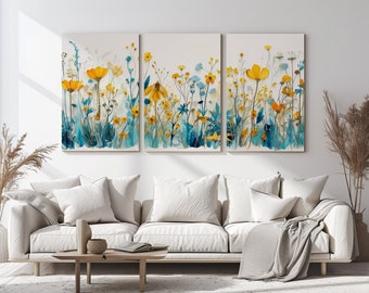 May include: A three-piece canvas wall art set featuring a watercolor painting of yellow and blue wildflowers. The artwork is displayed above a white couch in a living room setting.