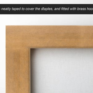 Puede incluir: Primer plano de la parte posterior de una obra de arte enmarcada. El marco de madera es de color marr&oacute;n claro. La parte posterior est&aacute; cuidadosamente encintada para cubrir las grapas y est&aacute; equipada con ganchos de lat&oacute;n. El lienzo es blanco.