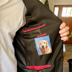 May include: The inside of a black suit jacket with a red lining. A small photo of a golden retriever dog is sewn into the inside pocket.