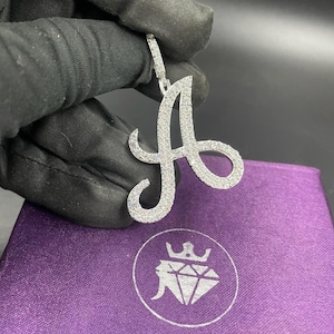 May include: A silver pendant in the shape of the letter A, encrusted with small, clear stones. The pendant is hanging from a silver chain.