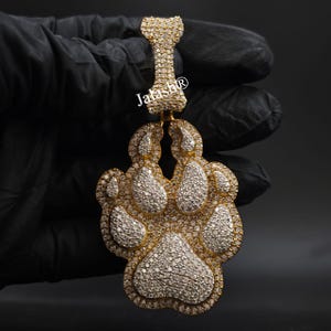 May include: A gold paw print pendant encrusted with clear cubic zirconia stones. The pendant is attached to a gold chain.