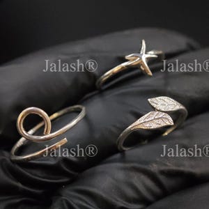 May include: Three silver rings displayed against a black background. One ring features a star design, another has a leaf design, and the third has a looped design. The rings are crafted with a shiny, metallic finish.