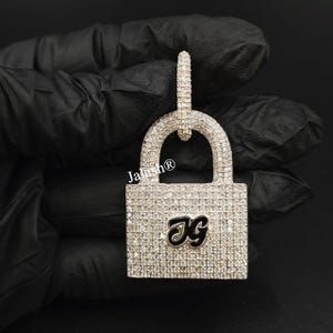 May include: A silver padlock pendant with a clear crystal design and the initials "JG" in black on the front.
