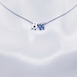 May include: A silver necklace with the initials "HW" in a minimalist font. The pendant is attached to a delicate chain, creating a simple and elegant design. The necklace is displayed against a white background.
