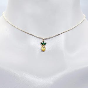 May include: A gold chain necklace with a small pineapple pendant featuring yellow and green crystal accents.