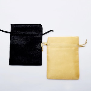 May include: Two small drawstring bags, one black and one beige, made of soft fabric. The bags are ideal for packaging small gifts or jewelry.
