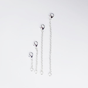 May include: Three silver extender chains of different lengths, each with a lobster clasp on one end and a jump ring on the other.