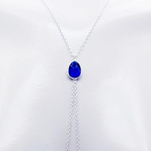 K&ouml;nnte beinhalten: Eine silberne Kettenkette mit einem tropfenf&ouml;rmigen blauen Edelstein-Anh&auml;nger. Die Kette ist unten verdoppelt und bildet zwei Str&auml;nge.