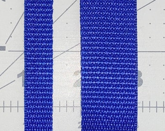 May include: Close-up of two strips of blue woven fabric. The fabric has a textured, ribbed appearance. The strips are vertical and parallel, with a light-colored surface in the background. The fabric appears to be a durable material, possibly for straps or belts.