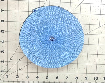 May include: A tightly coiled roll of light blue woven fabric. The circular shape reveals the spiral pattern of the material. The fabric appears to be a durable, possibly synthetic, material. The roll is centered on a grid.