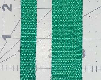 May include: Two pieces of green webbing, each about 1 inch wide, are shown side-by-side. The webbing is woven with a tight, even weave.