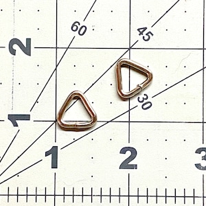 May include: Two silver triangle-shaped metal rings, approximately 1 inch in diameter, are shown on a white gridded surface. The grid is marked with numbers 1, 2, and 3, and lines marked with 30, 45, and 60.