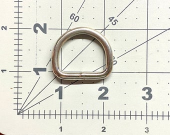 May include: A silver metal D-ring measuring approximately 1 inch in diameter. The ring is shown on a white grid background.