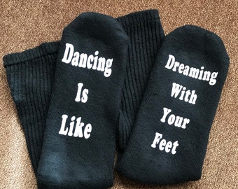 May include: A pair of black socks with white text. One sock says "Dancing is like" and the other sock says "Dreaming with your feet".