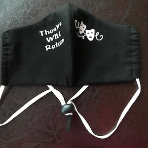 May include: Black face mask with white text that reads "Theatre Will Return" and two white theatrical masks on the right side. The mask has white ties.
