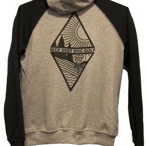 May include: A gray and black hooded sweatshirt with a diamond-shaped design on the back. The design features a sun, trees, a disc golf basket, and the text "NICE SHOT DISC GOLF".