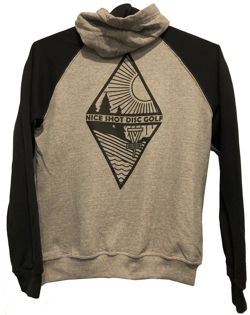 May include: A gray and black hooded sweatshirt with a diamond-shaped design on the back. The design features a sun, trees, a disc golf basket, and the text "NICE SHOT DISC GOLF".