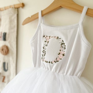 Op de afbeelding: Witte tule tutu jurk met een wit geribd tanktop met een geborduurde bloemletter D.