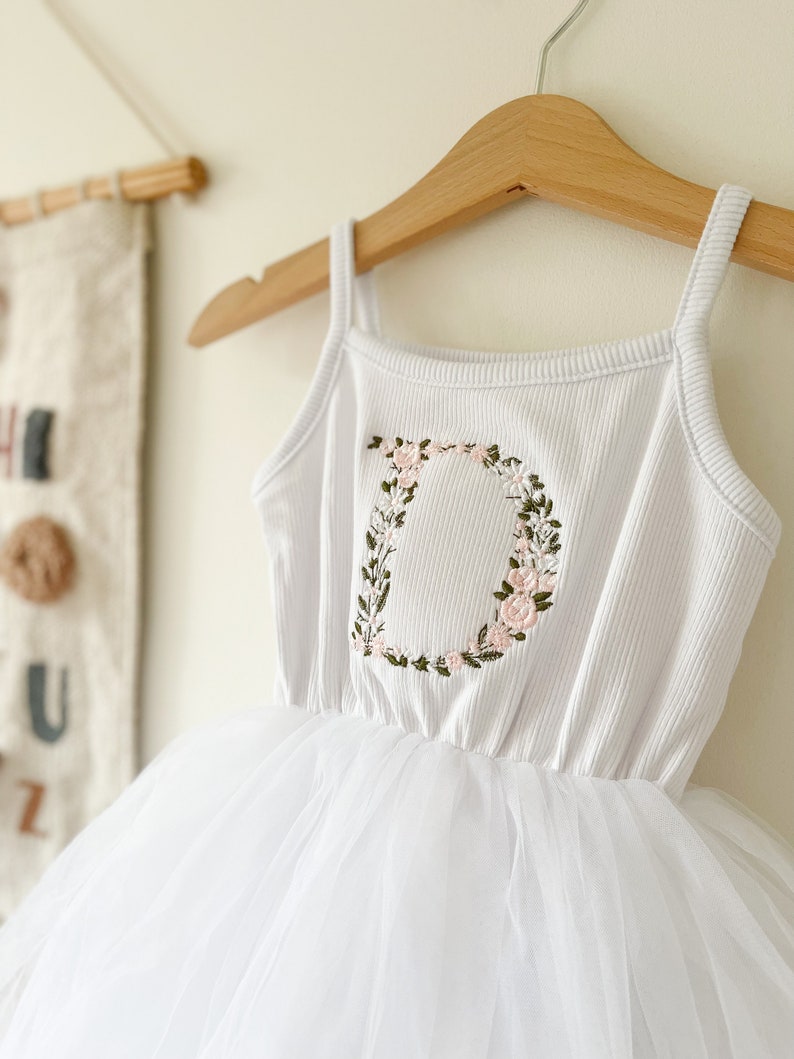 Op de afbeelding: Witte tule tutu jurk met een wit geribd tanktop met een geborduurde bloemletter D.