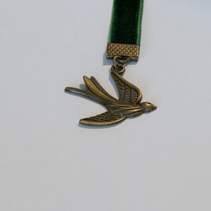 May include: A green velvet bookmark with a metal bird charm. The bird is in flight and has a detailed design.