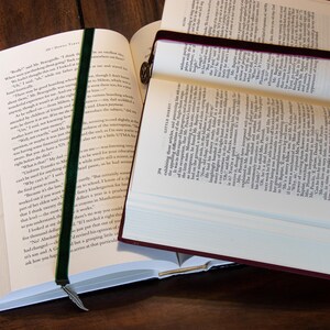 May include: Two open books with bookmarks. The book on the left has a green velvet bookmark with a feather charm. The book on the right has a burgundy velvet bookmark.