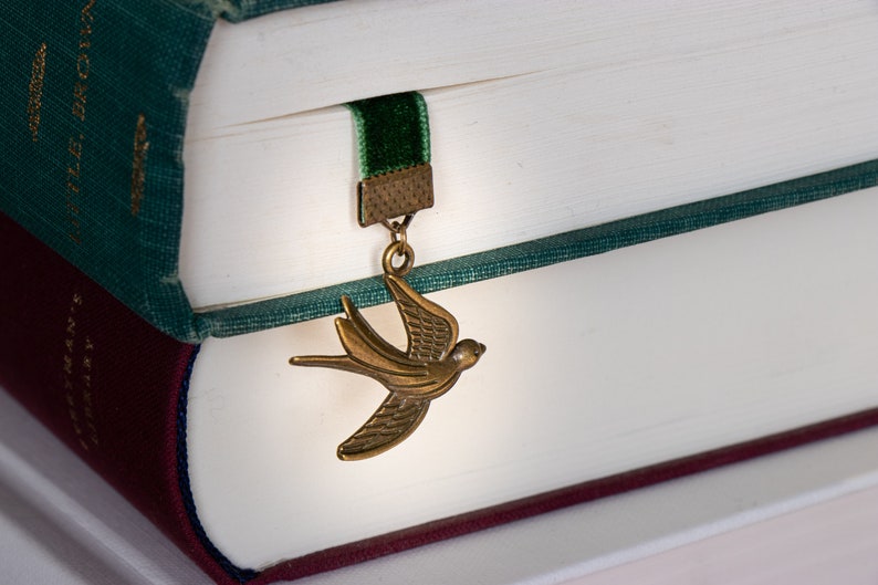 May include: A green and burgundy book with a green velvet bookmark. The bookmark has a gold metal charm shaped like a bird.
