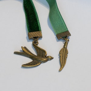 May include: Two green velvet ribbon bookmarks with metal charms. One charm is a bird and the other is a feather.