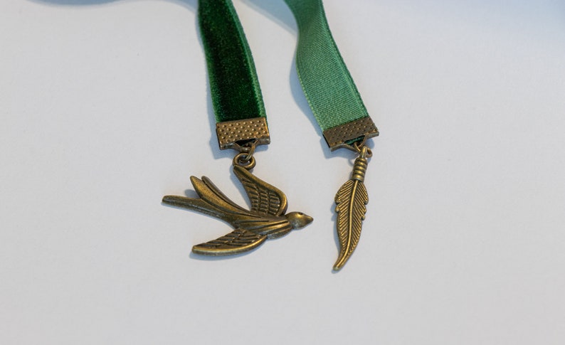 May include: Two green velvet ribbon bookmarks with metal charms. One charm is a bird and the other is a feather.