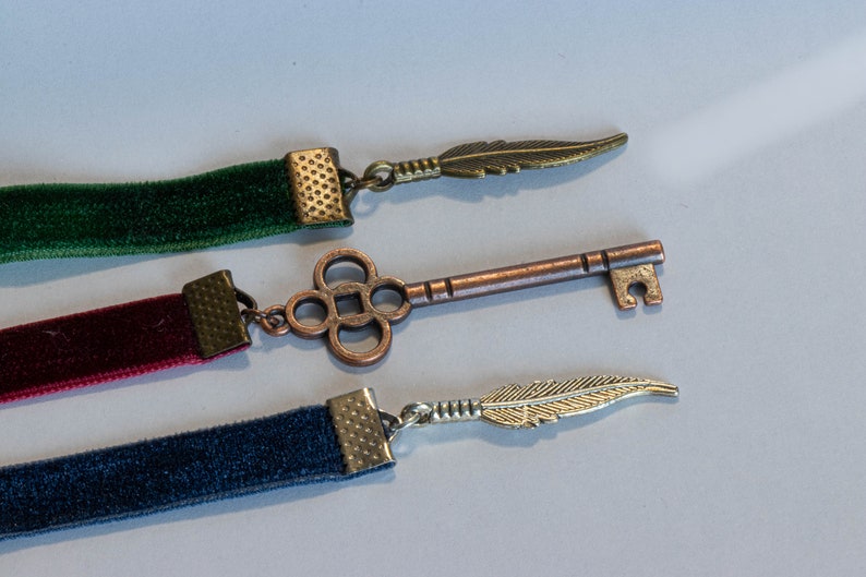 May include: Three velvet ribbon bookmarks with different colored ribbons and decorative metal charms. The charms include a feather, a key, and another feather.