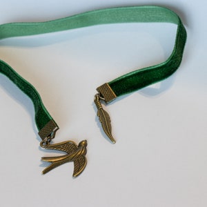 May include: A green velvet bookmark with a gold bird and feather charm.