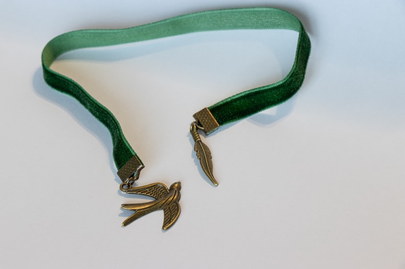 May include: A green velvet bookmark with a gold bird and feather charm.