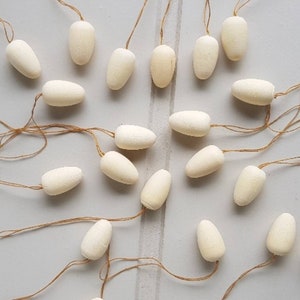 May include: A collection of 19 white, egg-shaped ornaments with string attached to each. The ornaments are hanging from a white surface.