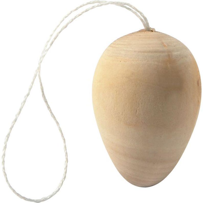 May include: A light-colored, wooden egg-shaped ornament with a white string attached at the top. The wood grain is visible on the surface of the egg. The string is made of twisted fibers.