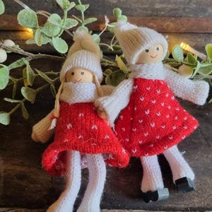 May include: Two handmade knitted dolls with white yarn hats and red yarn dresses with white polka dots. The dolls have painted faces and white yarn arms and legs.