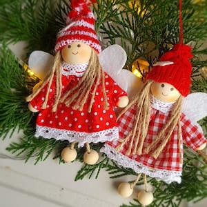 May include: Two red and white fabric angel ornaments with wings, brown yarn hair, and wooden beads for legs. The angels are wearing red and white polka dot and plaid dresses.