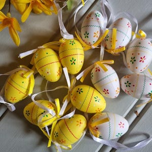 May include: A selection of Easter eggs in yellow and white, decorated with floral designs and ribbon ties. The eggs are about 7.6 cm tall, ideal for Easter celebrations and decorations.