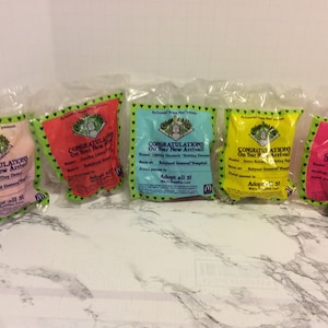 May include: Five colorful plastic bags with the words "Congratulations on your new arrival" and "Adopt all 51" printed on them. The bags are from the "Cabbage Patch Kids" brand and feature a cartoon baby on each bag.