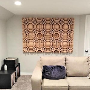 Könnte beinhalten: Ein beiges Sofa mit einem dunkelblauen Kissen vor einer Wand mit einer großen, hölzernen Akustikplatte. Die Platte besteht aus vielen kleinen Quadraten und Rechtecken, die ein geometrisches Muster bilden.