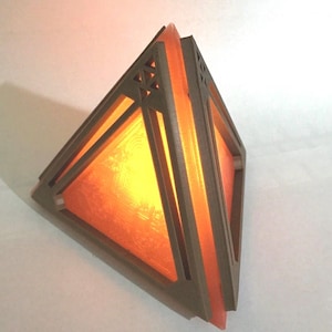 May include: A triangular wooden lamp with a geometric design and a warm orange glow. The lamp is made of multiple layers of wood, creating a layered effect.