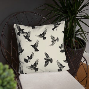 May include: A white throw pillow with a black and white pattern of birds in flight. The pillow is sitting on a black metal chair.