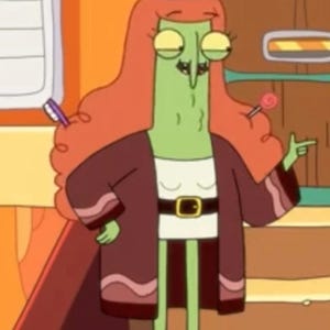 May include: A green cartoon character with red hair wearing a witch's hat and a brown robe with a gold belt. The character is holding a lollipop and pointing with their right hand.