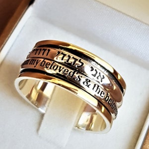 Puede incluir: Un anillo giratorio de plata y oro con las palabras hebreas "אהבה" y "אהובי" grabadas, que se traducen como "amor" y "mis amados".