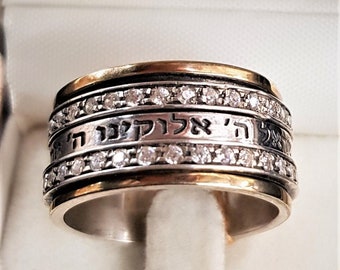May include: A silver and gold spinning ring with a Hebrew inscription and a row of small clear diamonds.