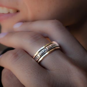 May include: A silver and gold spinning ring with Hebrew text inscribed on the band.