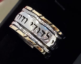 May include: A silver and gold spinning ring with Hebrew text that reads "לדוד" and "הודו" on the band.
