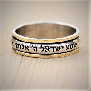 May include: A silver and gold spinning ring with Hebrew text that reads "Shema Yisrael Adonai Eloheinu Adonai Echad" which translates to "Hear O Israel, the Lord our God, the Lord is One".
