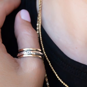 May include: A silver spinning ring with Hebrew text inscribed on the band. The ring is worn on a person's finger.